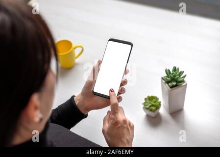 Frau mit smart phone mit isolierten Bildschirm für Mockup, Anwendung oder Website Präsentation. Schreibtisch mit Tasse Kaffee und Pflanzen ich Hintergrund Stockfoto