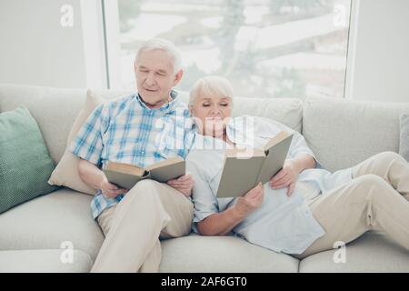 Portrait von ihr, dass sie Seine er zwei schöne attraktive Konzentrierte Stille Ehegatten divan Lesen neue interessante Buch sitzen in hellen weissen konzentrierten Stockfoto