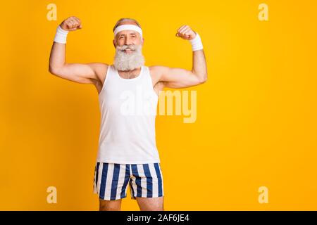 Isoliert Foto von stattlichen Fröhlicher positiver Mann alte lächelnd toothily zeigen Bizeps in der Nähe der leeren Raum leuchtend gelben Farbe Hintergrund Stockfoto