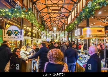 Mercado San Miguel in Madrid, Spanien ist besetzt mit Menschen. Eine Markthalle hier im Dezember gesehen mit festliche Weihnachten Girlanden schmücken die Balken. Stockfoto