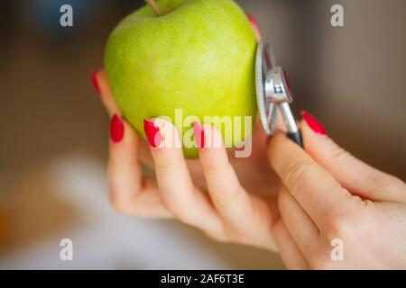 Gesundheit. Das gesunde Essen. Die Ernährungsberaterin hält in den Händen von frischen, grünen Apfel. Frisches Obst und Gemüse auf den Tisch. Gerne Arzt. Hohe Stockfoto