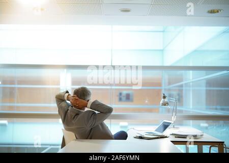 Rückansicht Blickrichtung der Geschäftsmann im Büro Stuhl gelehnt mit Arme hinter Kopf Stockfoto