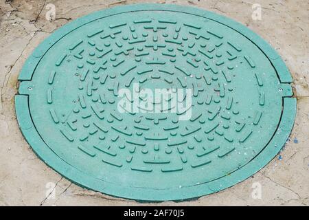 Geschlossene grüne Limousine von Abwasser im Außenbereich. Runder Deckel Gullideckel in Beton, Abwasserkanal Stockfoto