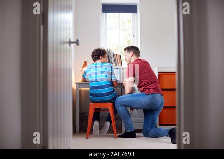 Blick durch die Tür als Vater hilft Sohn mit Laptop auf dem Schreibtisch zu tun Hausaufgaben Stockfoto