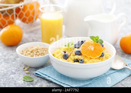 Mais Porridge mit frischen Heidelbeeren, orange und Pinienkernen in der Schüssel zum Frühstück serviert. Stockfoto