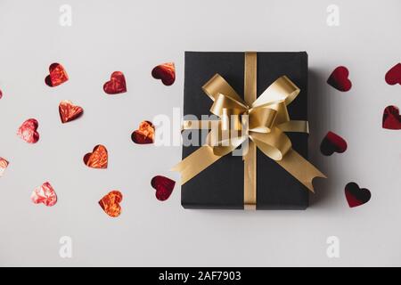 Urlaub Hintergrund. Handgefertigten Geschenkbox mit roten Herzen Konfetti auf grauem Hintergrund eingerichtet. Minimal Style und Valentines Tag Konzept. Flach, oben vi. Stockfoto