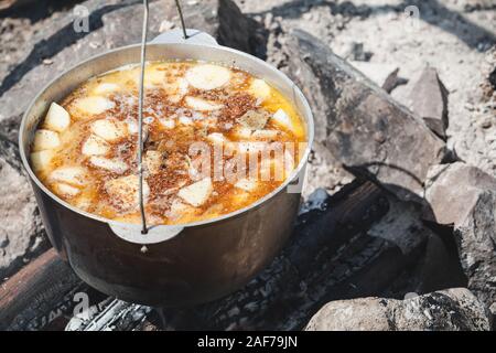 Würzige touristische Suppe mit Gemüse kocht in einem Kessel. Vorbereitung auf offenem Feuer, Camping Essen Stockfoto