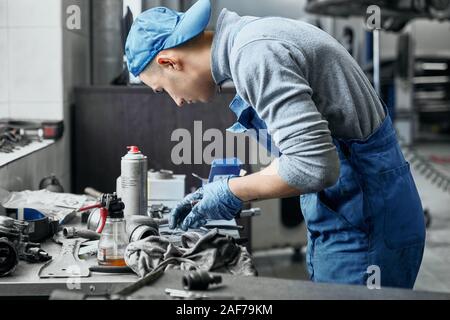 Seitenansicht des konzentrierten jungen Auto Service-Mitarbeiter arbeiten in der Nähe von Schreibtisch mit einer Vielzahl von Instrumenten an. Handwerker, Restaurierung von alten Details für Stockfoto