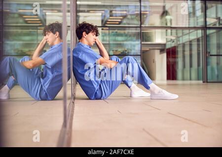 Müde Junge männliche Arzt tragen Scheuert sich gegen Wand im modernen Krankenhaus Gebäude Stockfoto