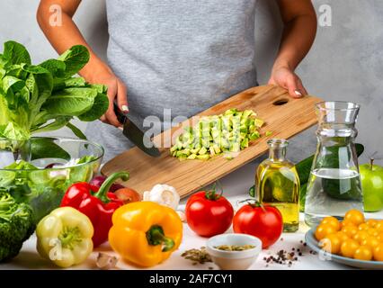 Avocado in Scheiben geschnitten auf einer Holzplatte in weibliche Hände. Frau ist Kochen Salat. Gesunde Ernährung Konzept. Stockfoto