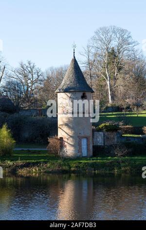 Alter Steinturm mit einem Taubenschlag oder Taubenschlag am Ufer eines Sees in einem ländlichen französischen Dorf in Creuse, Nouvelle-Aquitaine, Frankreich im Abendlicht Stockfoto