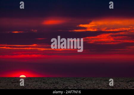 Schöne rote und orange Sonnenuntergang über dem Meer in einem bewölkten Himmel. Sonnenuntergang über dem Meer. Zwei Möwen fliegen gegen den Sonnenuntergang. Dramatische Sun Stockfoto