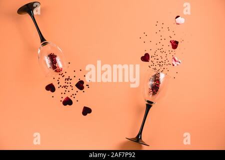 Zwei klirren Weingläser goß Rotes Herz Konfetti auf orange Farbe Papier Hintergrund. Minimalistischer Stil. Vorlage feminine Blog social media Postkarte Stockfoto