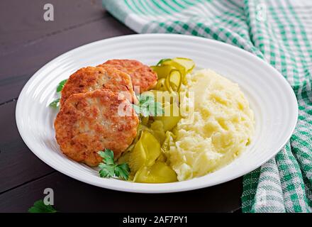 Hausgemachte gebratene Schnitzel/Frikadellen mit Kartoffelpüree und Gurken auf weiße Platte. Stockfoto