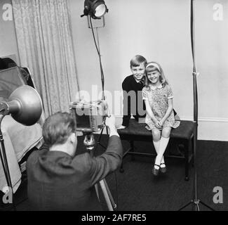 1960er Jahre, historisch, sitzen in einem Fotostudio, zwei Kinder, ein Bruder und eine Schwester, lassen sich von einem professionellen Fotografen mit einer Filmkamera auf einem Stativ fotografieren, England, Großbritannien. Stockfoto