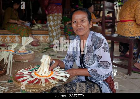 Lächelnd Balinesischen Frau in einem Batik Kleid und Blume Gaben an die Götter einen hinduistischen Tempel Stockfoto