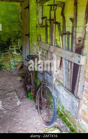 Eine rostige Oldtimer Fahrrad- und alte landwirtschaftliche Geräte in einer restaurierten Scheune in das verlassene Dorf Tyneham, Dorset, England, Großbritannien Stockfoto