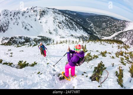 Frau hikeing in den verschneiten Bergen mit Telefon und Schneeschuhen. und Rucksack. Stockfoto