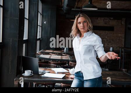 Fühlt sich schockiert. Geschäftsfrau mit lockigem Haar drinnen im Café zu Tagfahrlicht Stockfoto