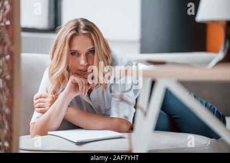 Liegend auf dem Sofa. Geschäftsfrau mit Lockigen, blonden Haaren sitzen im Zimmer gegen Fenster Stockfoto