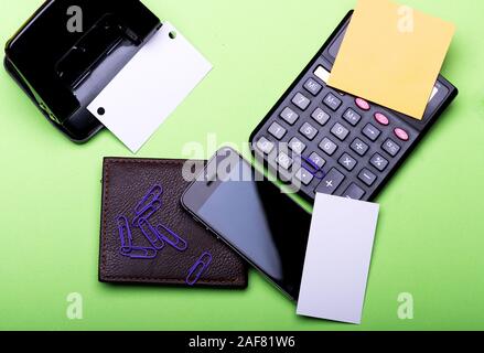 Schreibwaren, Geldbörse, Handy und Rechner. Visitenkarten mit Kopie Raum und Clips mit Aufkleber. Geldbörse, Handy und Lochung auf grünem Hintergrund. Business Accessoires und Gadgets Konzept. Stockfoto