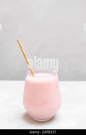 Glas Tasse indischen drink Erdbeer Lassi auf grauem Hintergrund mit Papier, Stroh Stockfoto