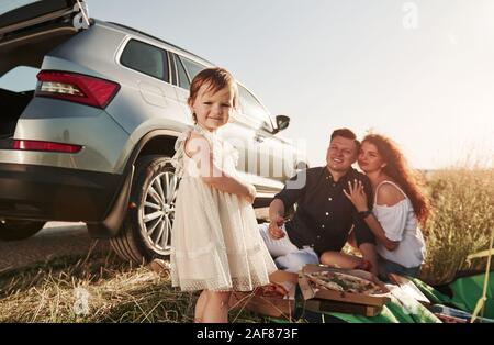 Kind im Zentrum der Aufmerksamkeit. Familie Picknick an Land in der Nähe von Silber Automobil bei Sonnenuntergang Stockfoto