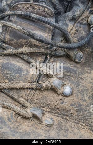 Nahaufnahme des schlammigen tappen Rinkes und Ösen auf ein Paar müde alte Wanderschuhe. Metapher Camping, Wandern/Wanderschuhe, das Leben im Freien. Stockfoto