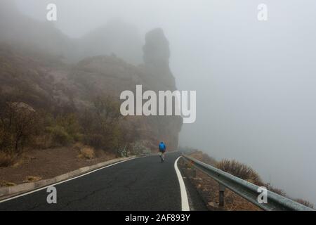 Person auf der Straße Fahrrad Radfahren bei schlechtem Wetter in den Bergen von Gran Canaria, Spanien (GC-60 in der Nähe von Ayacata) Stockfoto