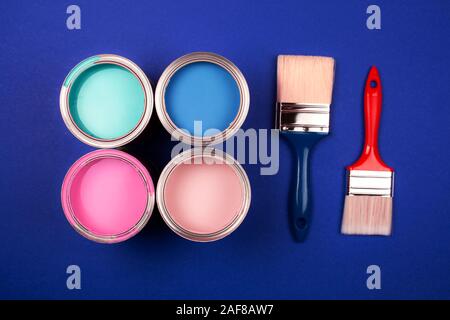 Vier offene Farbdosen mit Bürsten auf blauem Hintergrund. Gelb, Blau, Pink, Türkis Farben. Ansicht von oben. Stockfoto