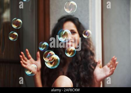 Cute girl spielt mit Blasen wie ein Kind. Schöne Frau mit lockigem Haar haben eine gute Zeit in der Stadt am Tag Stockfoto