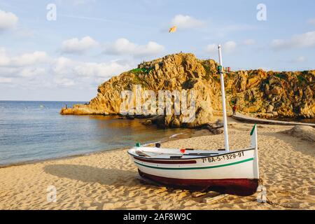 Traditionelle alte hölzerne Fischerboot auf dem felsigen Strand. Travel Concept. Costa Brava, Spanien. Fischerboot Rest am goldenen Sandstrand mit Blick auf die Stockfoto