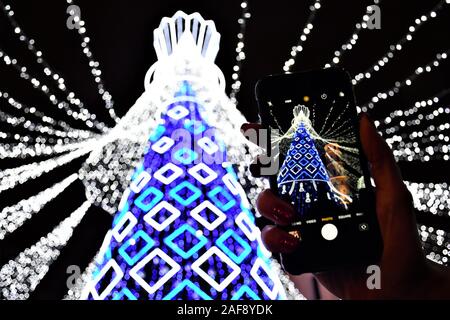 Weihnachtsbaum mit weißen und blauen Leds für Weihnachten 2019 und Neujahr 2020, Markt und Feiern in Vilnius, Mädchen Hand und Smartphone eingerichtet Stockfoto