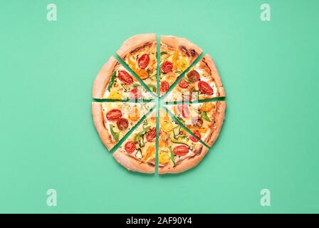 Ganze pizza Primavera in Scheiben geschnitten auf grünem Hintergrund. Oben Blick auf vegetarische Pizza. Italienische Küche. Pizza mit Tomaten. Hausgemachte Speisen. Stockfoto