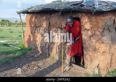 Tansania. Masai Mann verlassen sein Haus im Dorf Ololosokwan, nördliche Serengeti. Stockfoto