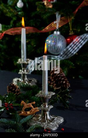 Brennende Kerzen in Antik Silber Kerzenleuchter mit geschmückten Weihnachtsbaum im Hintergrund. Stockfoto