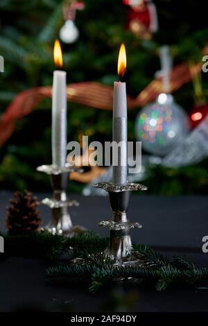 Brennende Kerzen in Antik Silber Kerzenleuchter mit geschmückten Weihnachtsbaum im Hintergrund. Stockfoto