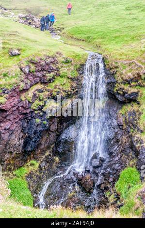 Wanderer Ford einen Datenstrom über einen Wasserfall über Klippen bei eshaness oder Esha Ness in Northmavine, Shetland. Stockfoto
