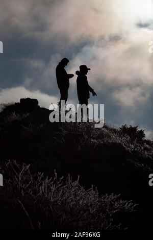 Silhouetten von zwei bergwanderer auf dem Peak durch gefrorenes Gras vor dem Hintergrund des blauen Himmels abgedeckt Stockfoto