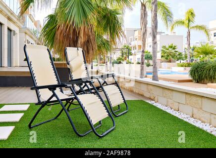 Zwei Lounge-Stühle auf Kunstrasen im Inneren der privaten Wohn-Sommervilla im Hinterhof, Blick auf moderne Häuser mit Schwimmbad, Spanien Stockfoto