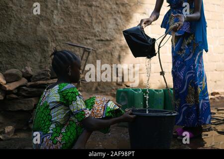 Nahaufnahme von afrikanischen schwarzen Kinder gießen Wasser aus einem Brunnen in den Eimer Stockfoto