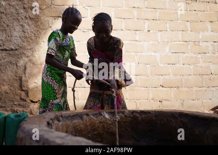 Silhouette Schuß von zwei afrikanischen Mädchen Sammeln von Wasser aus einem Brunnen Stockfoto