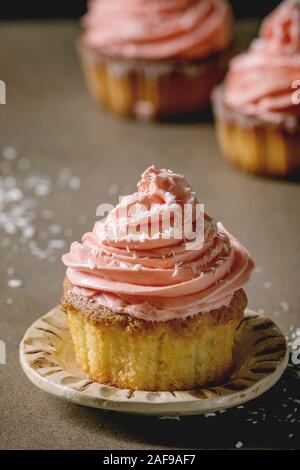 Hausgemachte Muffins mit Rosa buttercream und Kokosraspeln auf Keramikplatte auf dunklen Tisch serviert. Nahaufnahme Stockfoto