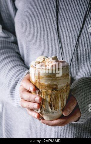 Frau im grauen pullover halten Sie in Händen Keramik Becher mit heißer Schokolade oder Kakao mit Marshmallow. Stockfoto