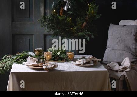 Weihnachten oder Neujahr Tisch mit leeren keramische Platten, Servietten, Weihnachten thuja Kranz, leuchtende Girlande und brennende Kerzen auf weißen tableclo Stockfoto