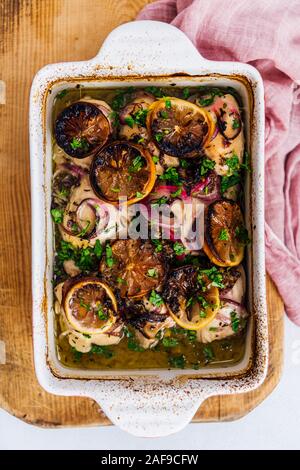 Gebackene Hühnerkeule mit Zitrone, Knoblauch Zwiebeln in eine Backform von oben Blick auf einem holzbrett fotografiert. Stockfoto