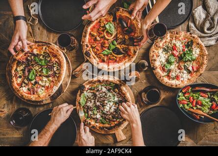 Familie oder Freunde in Pizza Party Abendessen. Flachbild-lay von Menschen und verschiedene Arten von Pizza essen und trinken Rotwein über rustikal Tabl Stockfoto