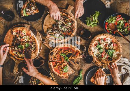 Familie oder Freunde in Pizza Party Abendessen. Flachbild-lay von Menschen essen verschiedene italienische Pizza und trinken Wein über Holz- Tabelle, Ansicht von oben. F Stockfoto