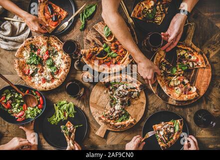 Familie oder Freunde in Pizza Party Abendessen. Flachbild-lay von Menschen essen verschiedene italienische Pizza, Salat, Wein trinken und über Holz- Tabelle, zu Stockfoto