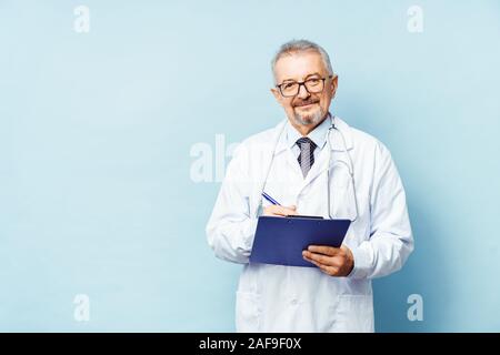 Lächelnd medizinische leitender Arzt mit einem Stethoskop. Auf einem blauen Hintergrund. Der Arzt hält die Ordner in der Hand und macht einen Termin in der Klinik Stockfoto
